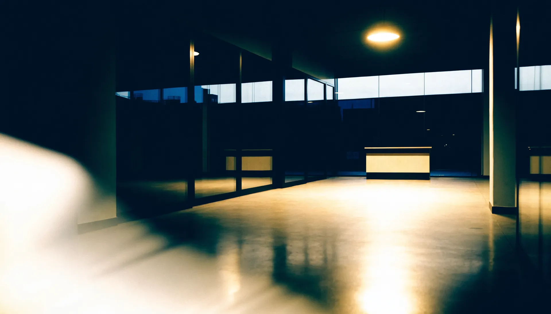 Leerer Ausstellungsraum eines Autohauses bei Nacht, eine einzelne Deckenleuchte über dem Tresen.